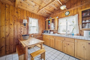 Cocina de cabaña de madera con una mesa, un banco, armarios, un microondas y un lavamanos.