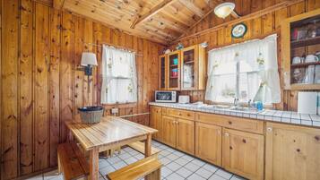 Un interior de madera con una zona de cocina que incluye una mesa de madera, un banco, armarios y un microondas.