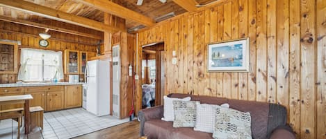 A wooden interior with a kitchen, dining area, and a living room with a sofa and pillows.
