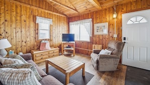 Un intérieur en bois avec un canapé, un fauteuil, un téléviseur et une porte blanche.