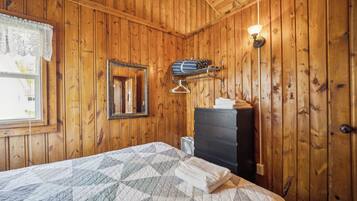 Une pièce aux murs lambrés, comprenant un lit, une commode, un miroir et une lampe fixée au mur.