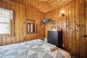 Una habitación con paneles de madera, una cama, un tocador, un espejo y una lámpara en la pared.