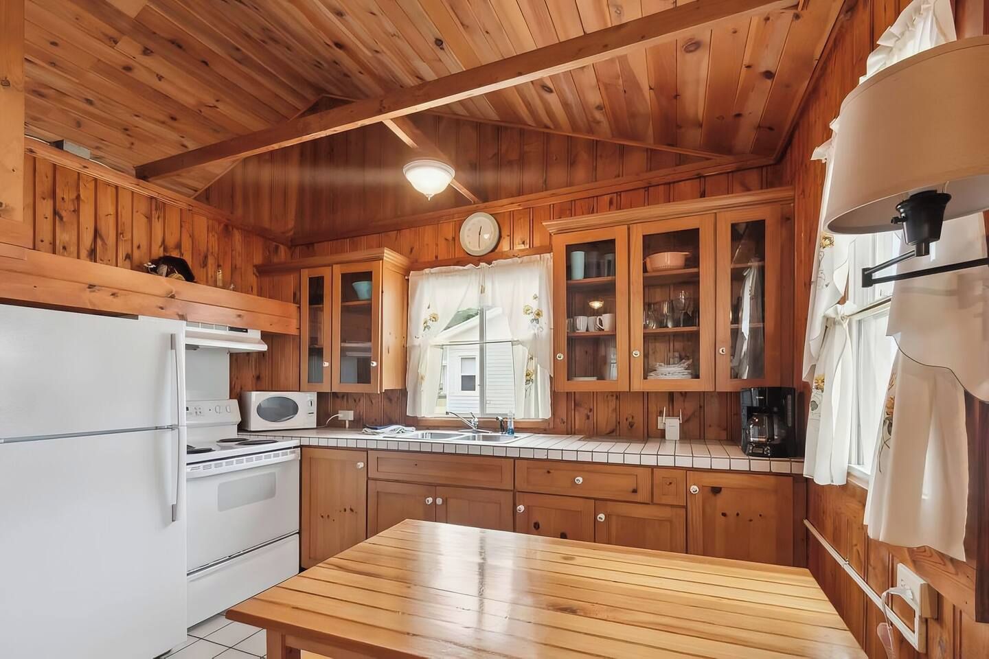 A wooden cabin-style kitchen with a refrigerator, stove, microwave, and cabinets.