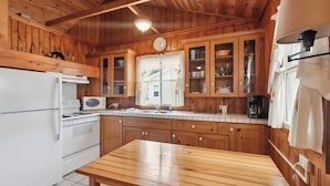 Een keuken in chaletstijl met een koelkast, fornuis, magnetron en kasten.