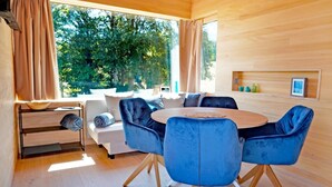 A modern room with a round wooden table, blue velvet chairs, a sofa, and a large window with curtains. - Ferienhaus, Sankt Georgen (Sankt Georgen OT Langenschiltach)