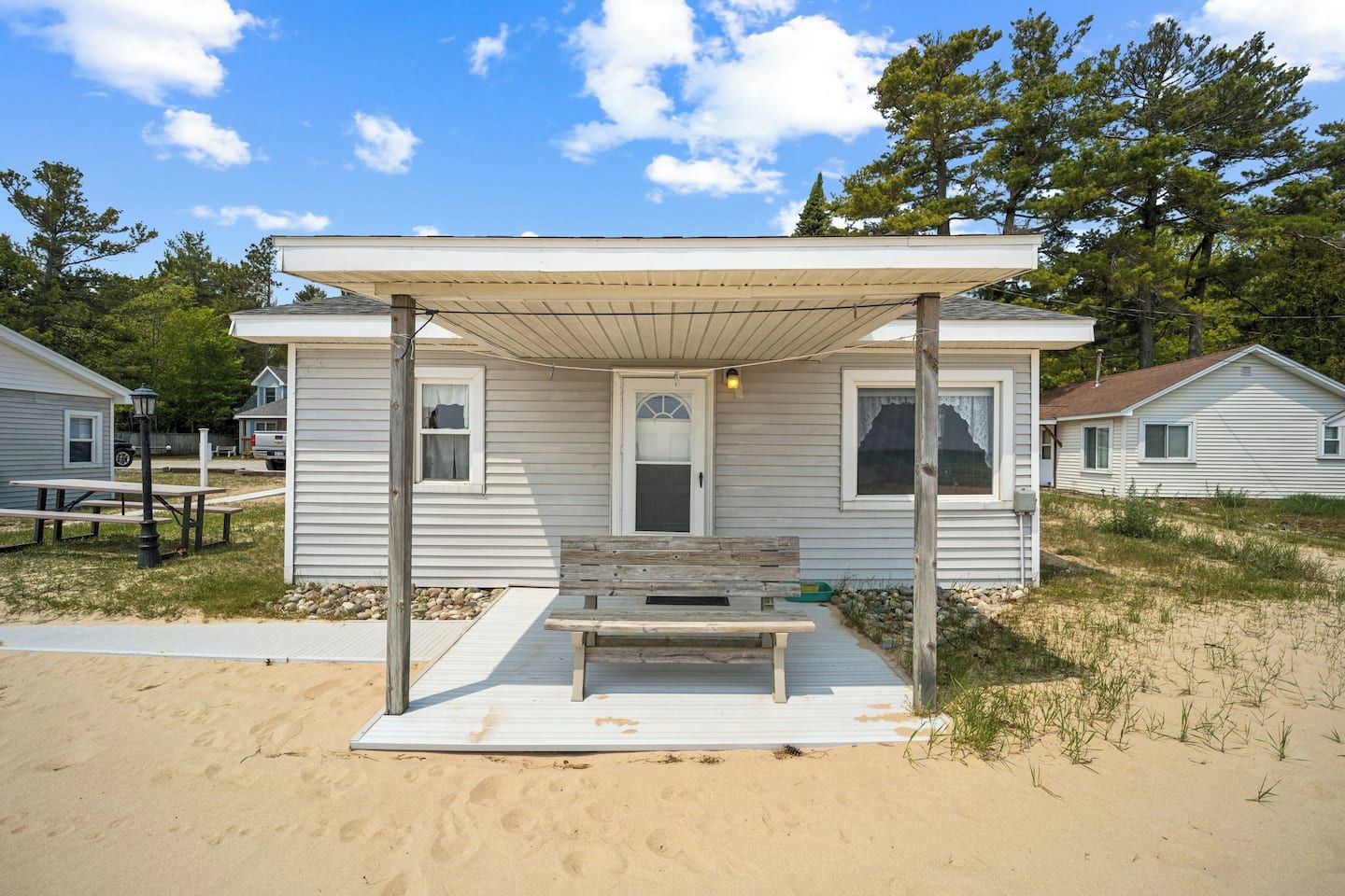 Una casa sulla spiaggia con un portico coperto, una panchina e un tavolino.
