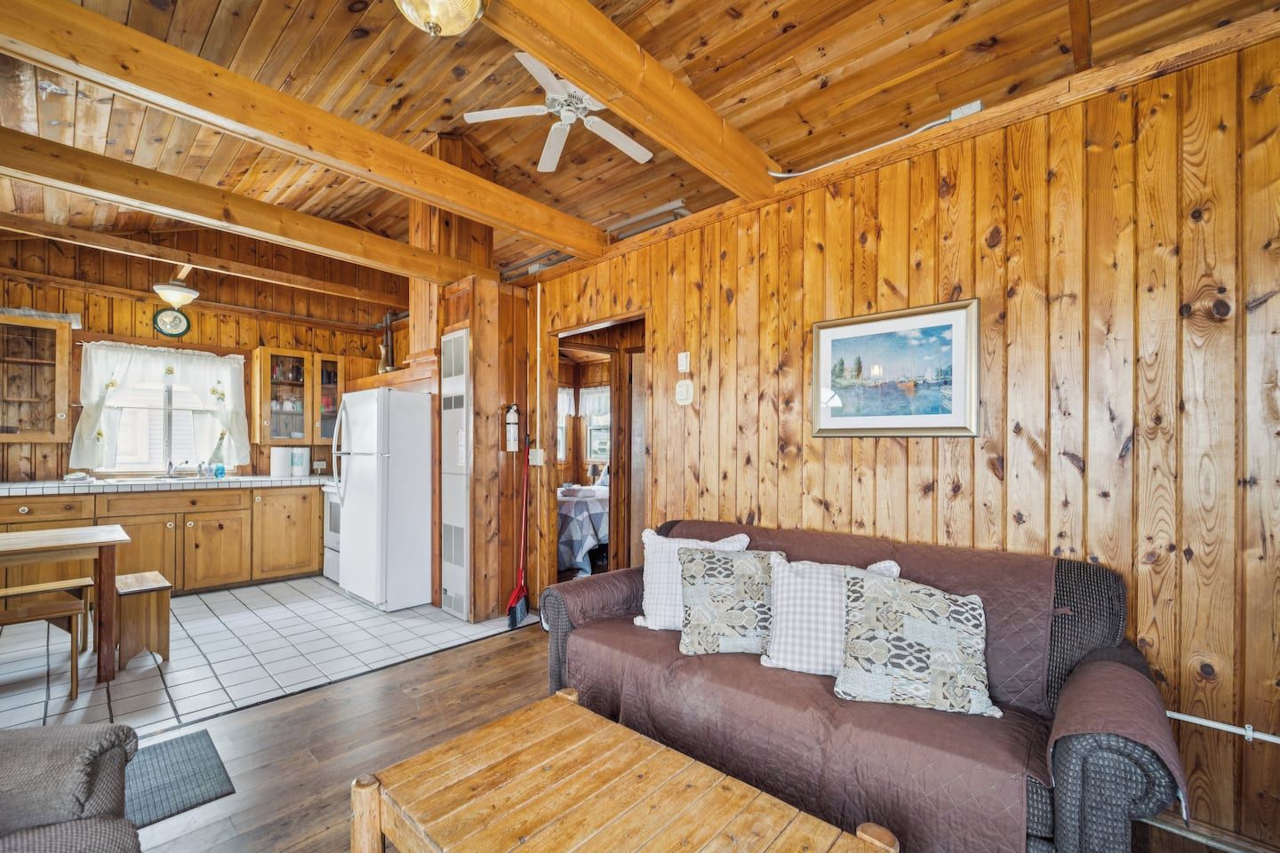 A wooden cabin interior with a kitchen, dining area, and a sofa with decorative pillows.