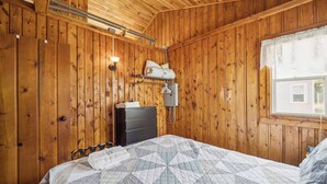 Puupaneloitu huone, jossa on sänky, lipasto, lamppu ja ikkuna.
