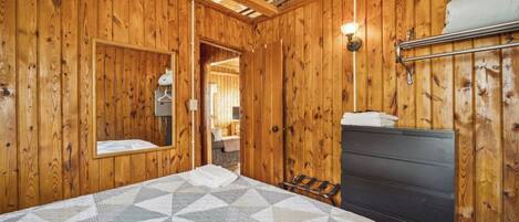 A wooden-paneled room with a bed, a nightstand, a wall-mounted lamp, and a mirror.