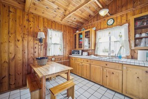 A wooden cabin-style kitchen with a wooden table, bench, cabinets, and a microwave.