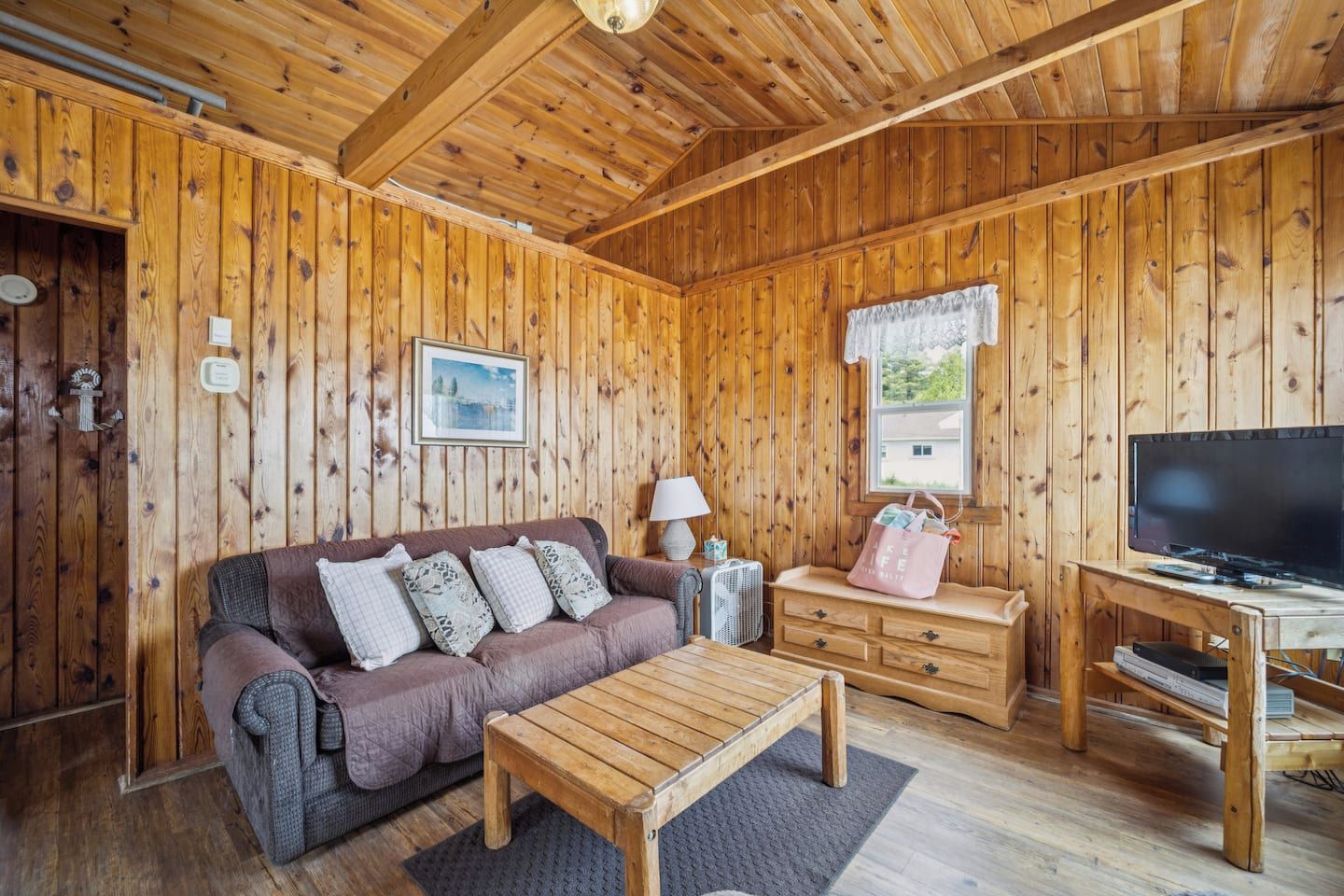Una habitación con paneles de madera, un sofá, una mesa de centro, un televisor y una ventana con vistas.
