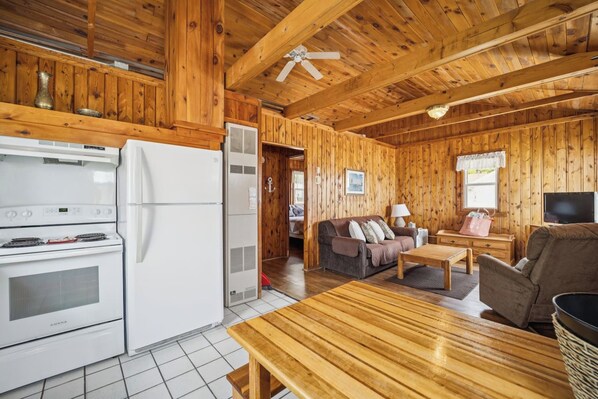 Un intérieur en bois comprenant un espace cuisine équipé d’une cuisinière, d’un réfrigérateur et d’une table à manger avec des chaises.