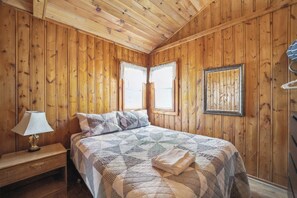 Een kamer met houten lambrisering, een bed, een nachtkastje, een lamp en een lijst met een afbeelding aan de muur.