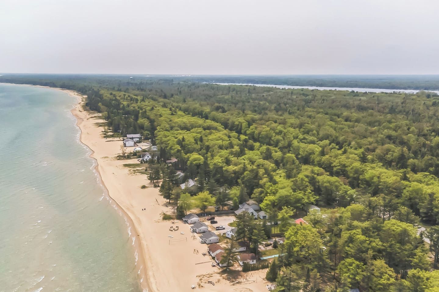 Vista aerea di una spiaggia con case lungo la costa e una fitta foresta sullo sfondo.