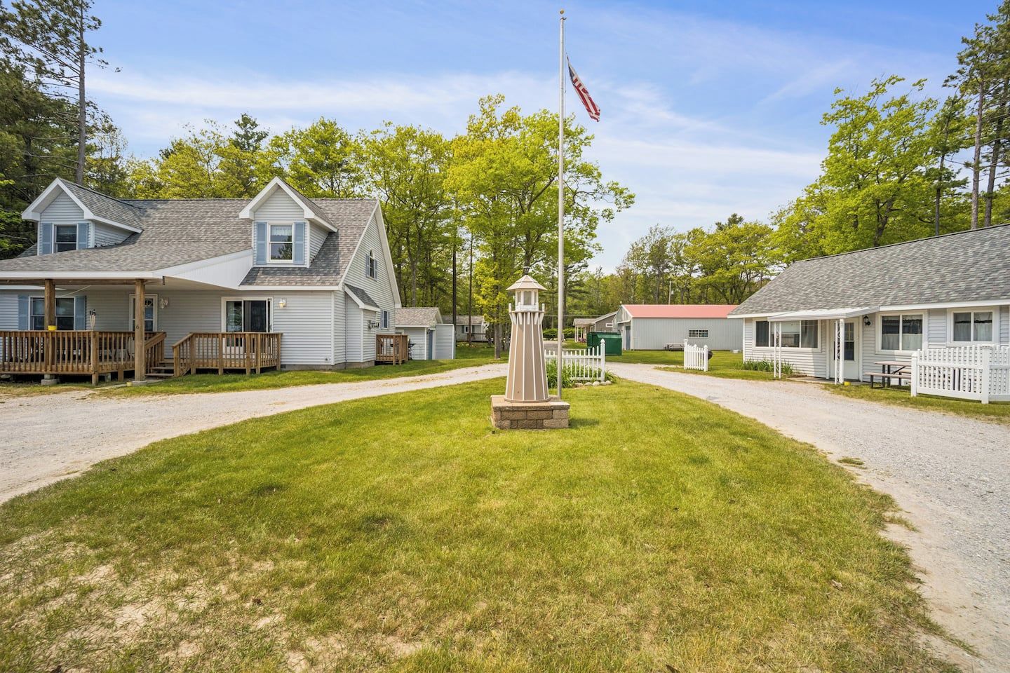 A row of single-story houses with a central flagpole, a gravel driveway, and a grassy lawn.