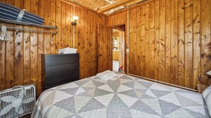 Ett rum med träpanel på väggarna, en säng, en byrå, en fläkt och en lampa.