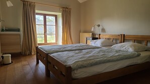 A bedroom with two wooden beds, a window with curtains, a bedside table with a lamp, and a radiator.