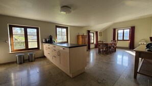 A spacious kitchen with a central island, large windows, and a dining area with chairs and a table.