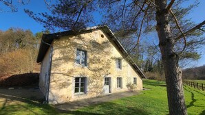 A stone house with a sloped roof, a small porch, and a window with shutters.