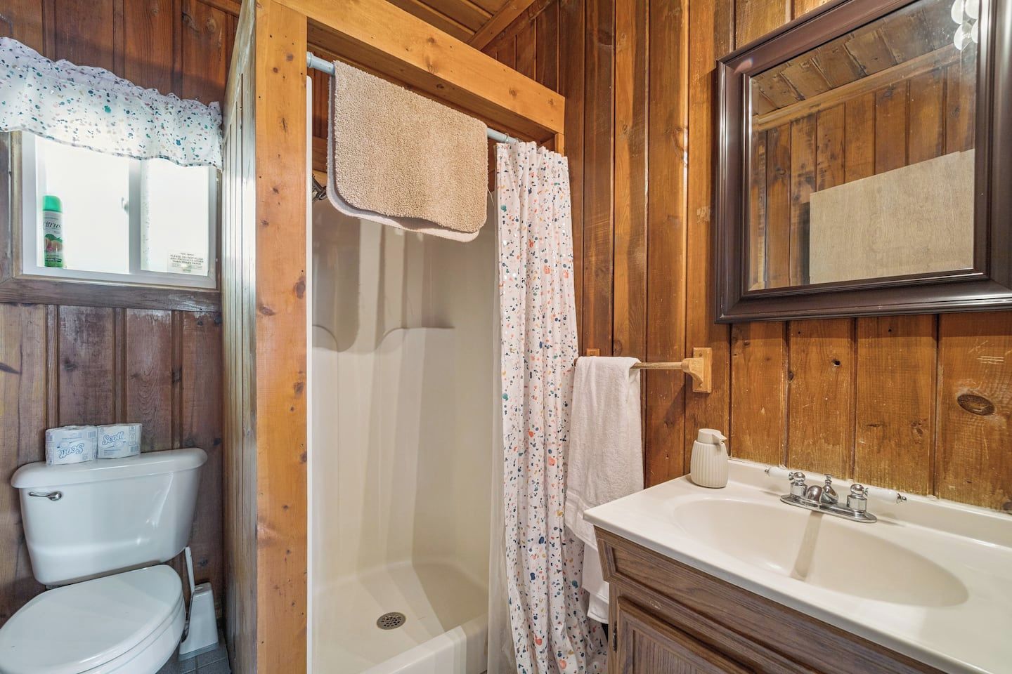 A wooden bathroom with a toilet, shower, and sink.