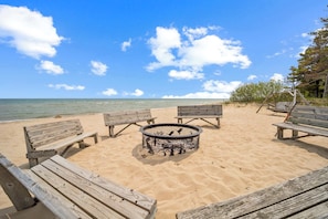 A beach setting with wooden benches and a fire pit. - Spacious Lakefront Cottage w/ AC (Greenbush)