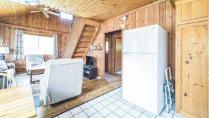 En stuga med träinredning, innehållande ett matområde, en soffa, en tv, ett kylskåp och en trappa.