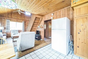 Een houten cabin met een eethoek, een bank, een televisietoestel, een koelkast en een trap.