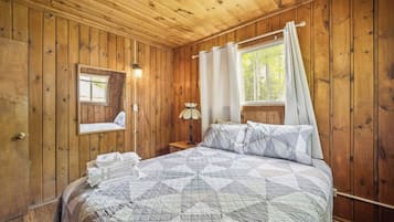Camera da letto in una baita di legno con un letto, un comodino, una lampada e una finestra con tende.
