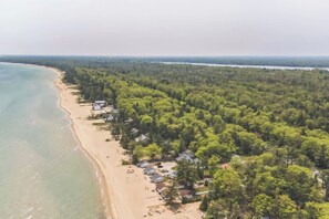 An aerial view of a coastal area with a sandy beach, dense forest, and several buildings. - 3BR/1BA lakefront cottage at Sunnyside with A/C, private beach access, and lawn games. (Greenbush)