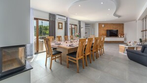 Un espace de salle à manger moderne, avec une grande table dressée pour six personnes, entourée de chaises en bois dotées de coussins noirs.