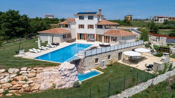 Une villa à plusieurs étages dotée d’une piscine, d’un espace salon extérieur et d’un jardin aménagé.