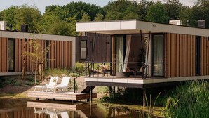 A modern houseboat with a deck, outdoor seating, and a view of a lake. - Water Lodge in Netherlands with Paddleboarding (Zeewolde)