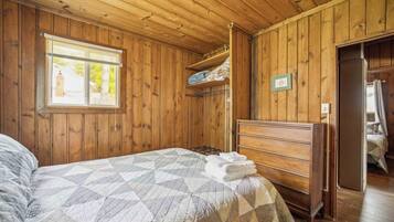 Ein Zimmer mit Holzwänden, einem Bett, einem Schminktisch und einem Fenster mit Jalousien.
