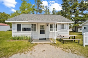 Une petite cabane à un seul étage, dotée d’un porche à l’avant, d’une table de pique-nique et d’une porte avec une fenêtre.