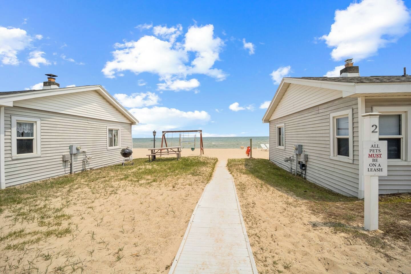 A pathway leading to beachside cabins with a sign indicating pets must be on a leash.