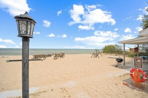 Une plage avec un espace équipé de bancs en bois, un barbecue et une bouée de sauvetage.