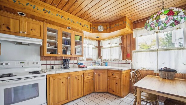 A kitchen with wooden cabinets, a white stove, and a dining area with a table and chairs.