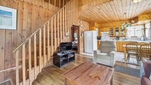 A wooden interior with a staircase, a living area with a TV and seating, and a kitchen with wooden cabinets.
