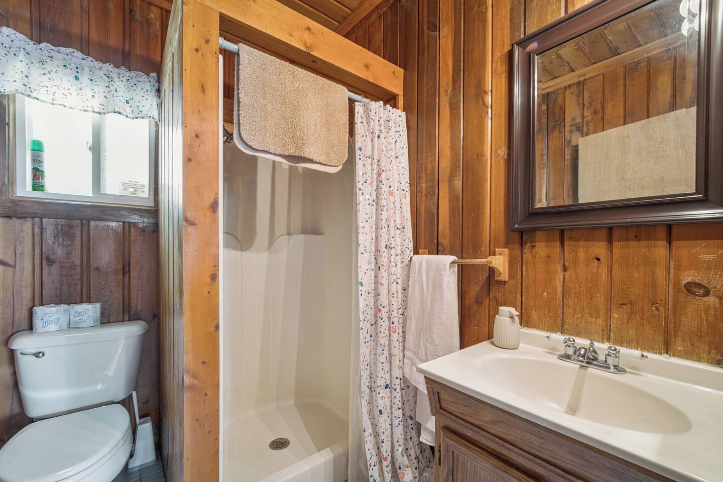 Un baño de madera con inodoro, ducha y lavamanos.