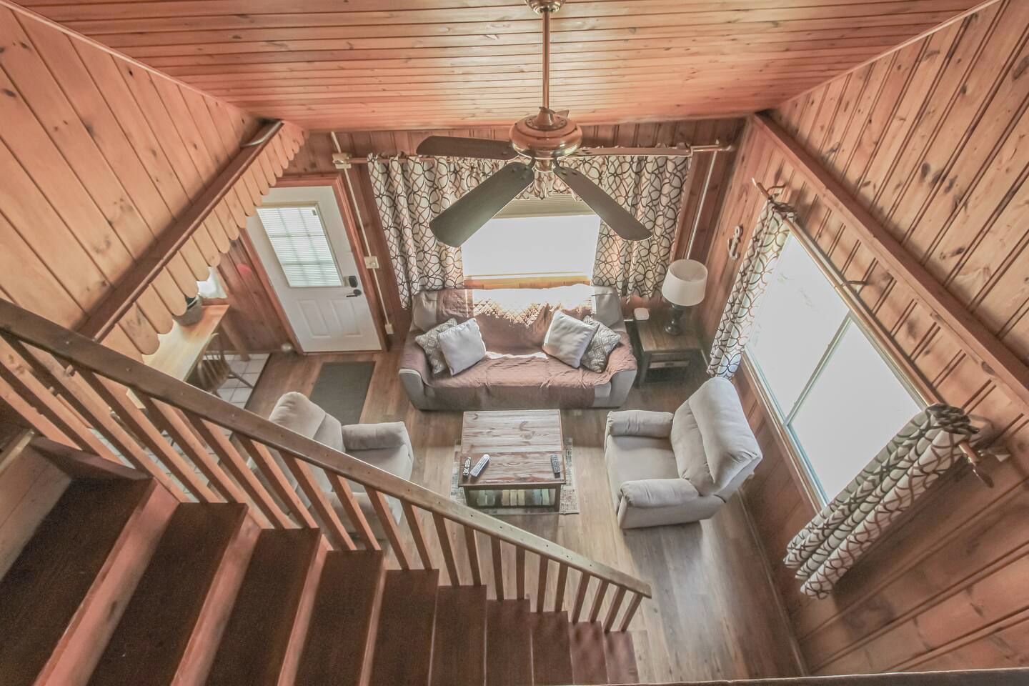 Ein Holzinnenraum mit einer Treppe, einer Sofagarnitur, einem Couchtisch und einem Deckenventilator.
