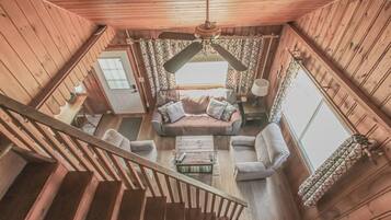 Ein Holzinnenraum mit einer Treppe, einer Sofagarnitur, einem Couchtisch und einem Deckenventilator.