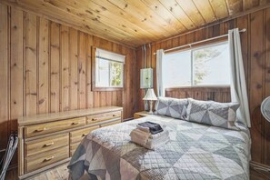 Une pièce aux murs lambrissés, comprenant un lit, une commode, une fenêtre et une lampe.