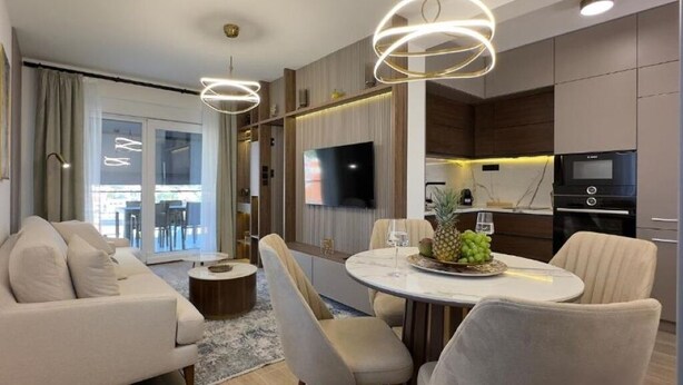 A modern living room with a sofa, a dining table with chairs, and a kitchen area with appliances.