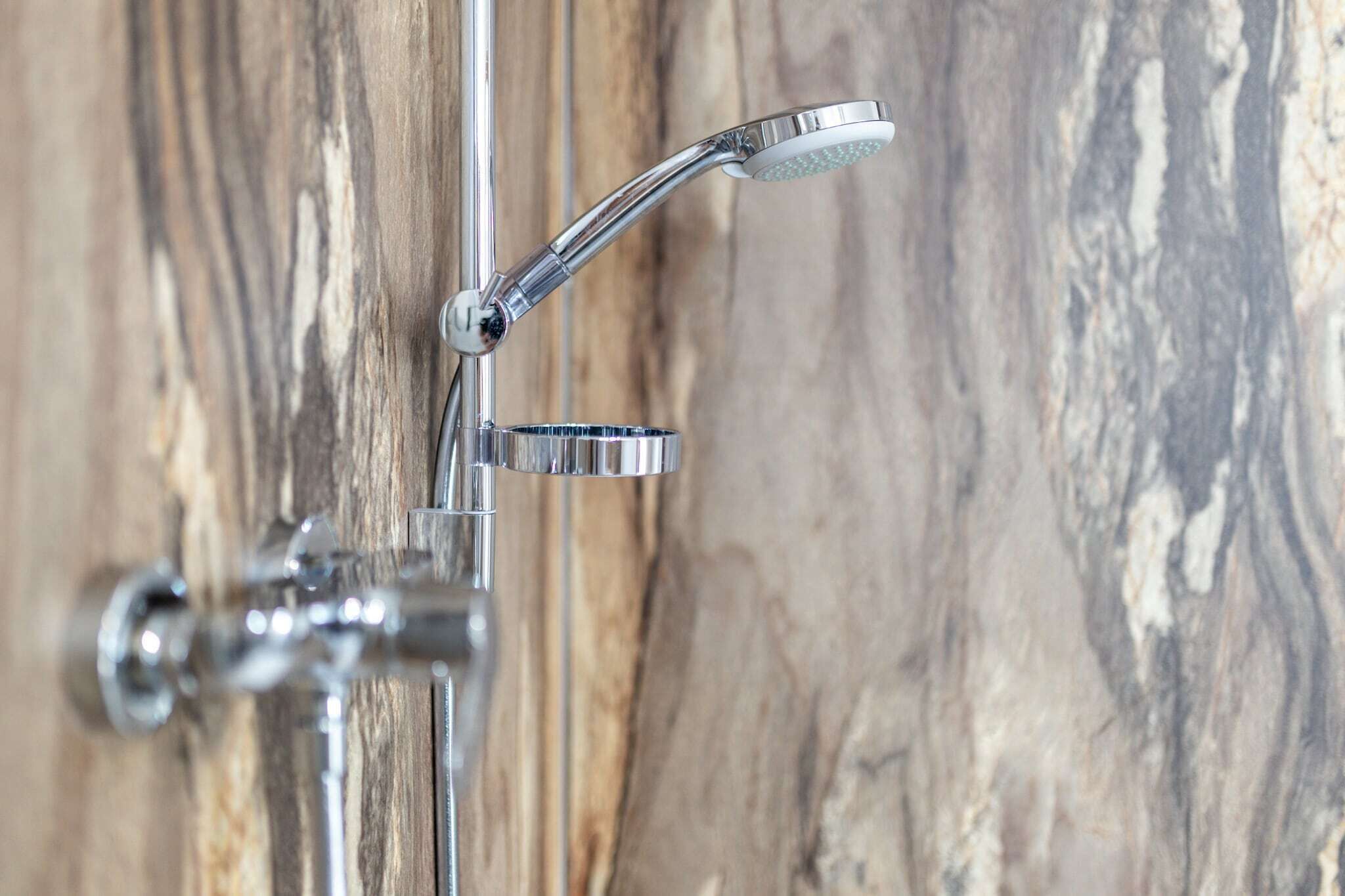 A chrome showerhead mounted on a wall with a wooden background.