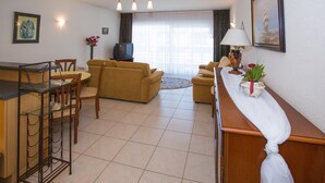 A living room with a sofa set, a dining table with chairs, a TV, and a lamp. - Partial Sea View Apartment (Middelkerke)