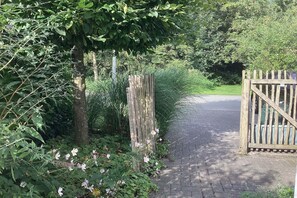 Enter a serene estate through this rustic wooden gate, surrounded by lush greenery and a well-manicured path.
