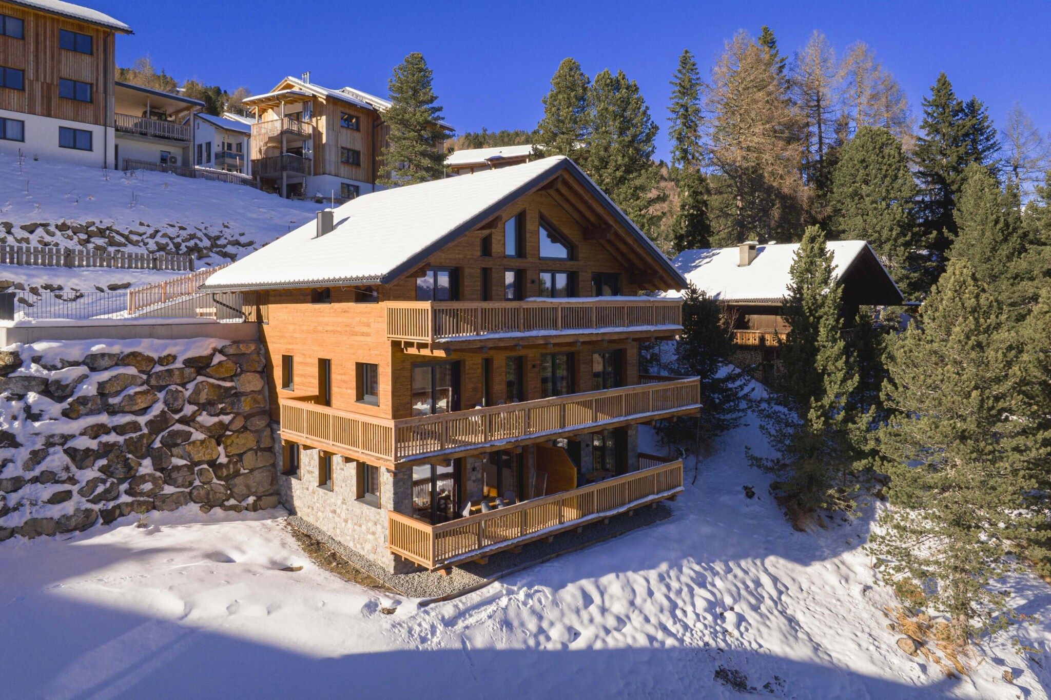 A multi-story wooden lodge with balconies, surrounded by snow and trees.