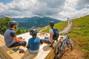 Three people sitting on wooden benches overlooking a mountain trail.
