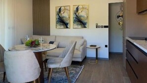 Een moderne eetruimte met een ronde tafel, stoelen en een bank. Er hangen abstracte schilderijen aan de muur en staat een klein bijzettafeltje.