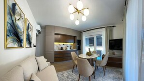 Een moderne woonkamer met een bank, een eettafel met stoelen, een keuken en een televisie die aan de muur is bevestigd.